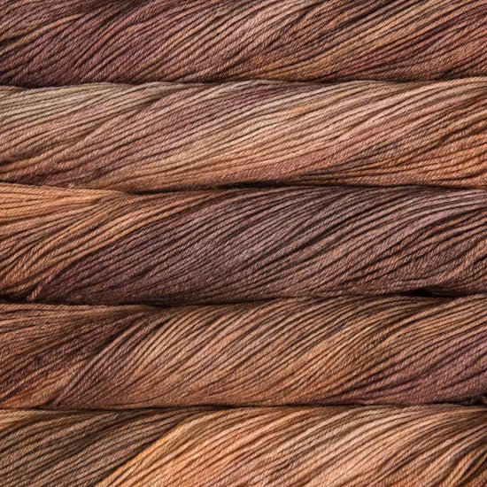 A close-up texture shot of Malabrigo Arroyo in color Coffee Toffee stacked yarn skeins in a variegated blend of earthy brown, rust, and tan tones.